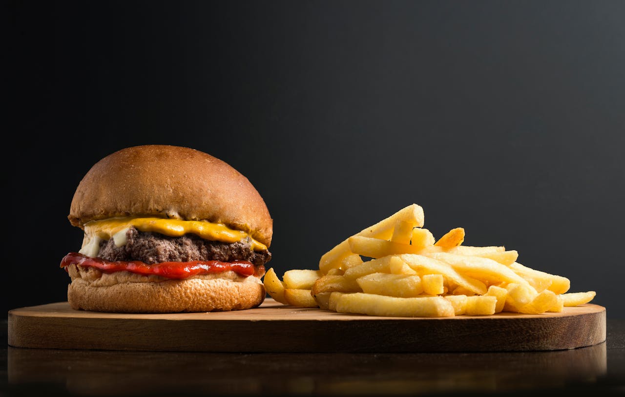 Home Appetizing burger with meat patty ketchup and cheese placed on wooden table with crispy french fries against black background