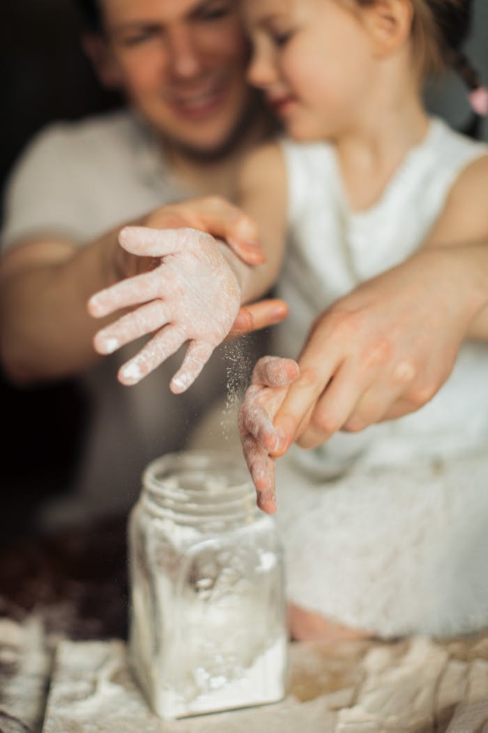 Services Happy crop cute girl with pigtail and blurred father shaking off flour from hands while making dough