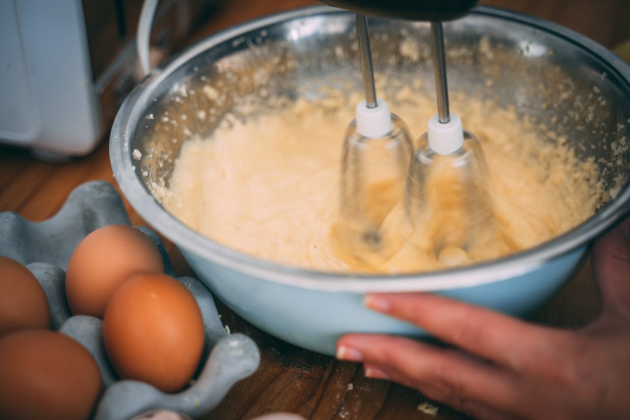Home Close-up of batter being mixed in a bowl with eggs nearby on a wooden table.